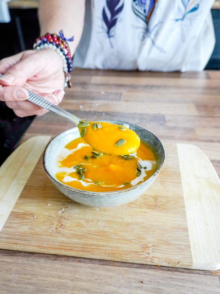 Bol de soupe potimarron carottes avec une main qui se sert à l'aide d'une cuillère